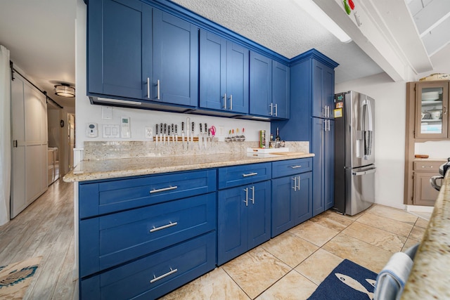 kitchen with a textured ceiling, light stone countertops, stainless steel fridge with ice dispenser, and blue cabinets