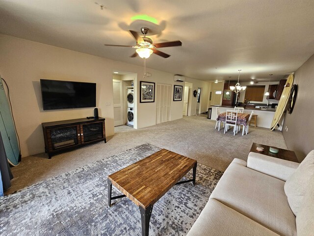 carpeted living room with ceiling fan with notable chandelier and stacked washing maching and dryer