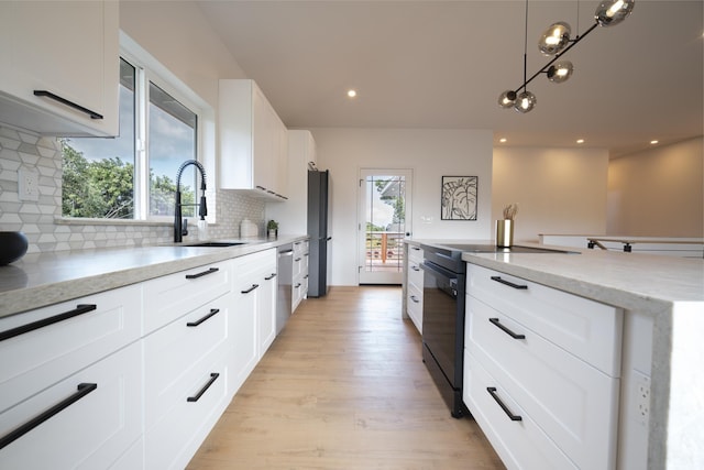 kitchen featuring light stone counters, a sink, white cabinets, black appliances, and decorative light fixtures