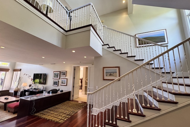 stairway with recessed lighting, a high ceiling, and wood finished floors