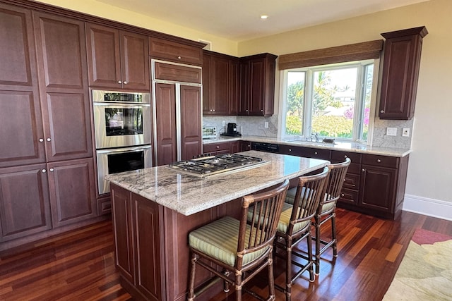 kitchen with decorative backsplash, appliances with stainless steel finishes, a breakfast bar area, and dark wood-style flooring