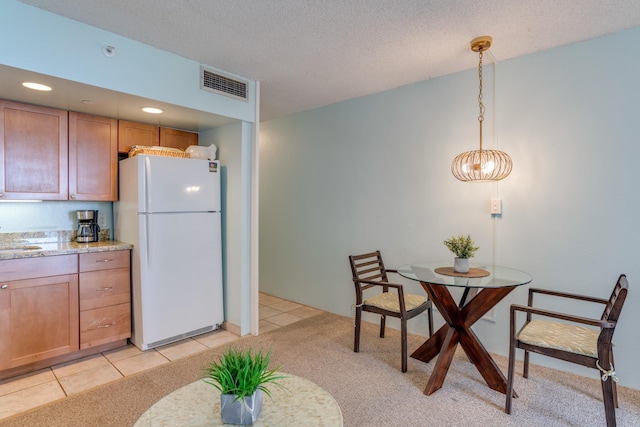 kitchen with light stone countertops, white fridge, sink, hanging light fixtures, and light tile patterned flooring