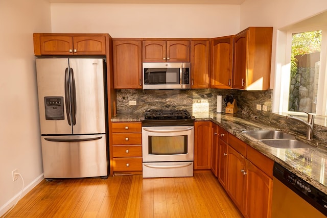 kitchen featuring backsplash, sink, light wood-type flooring, stainless steel appliances, and dark stone counters