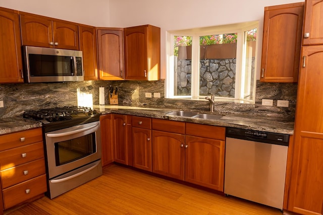 kitchen with tasteful backsplash, stainless steel appliances, dark stone countertops, sink, and light hardwood / wood-style flooring