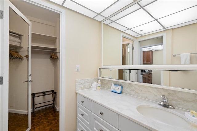 bathroom with a walk in closet, baseboards, and vanity