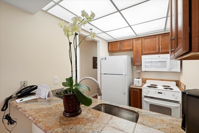 kitchen featuring brown cabinetry, light stone countertops, a sink, and white appliances