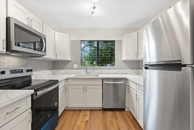 kitchen featuring appliances with stainless steel finishes, decorative backsplash, light hardwood / wood-style floors, white cabinetry, and sink