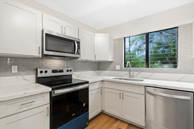 kitchen with white cabinetry, light stone countertops, stainless steel appliances, light wood-type flooring, and sink