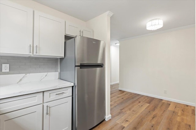 kitchen featuring ornamental molding, white cabinetry, stainless steel refrigerator, light hardwood / wood-style floors, and decorative backsplash