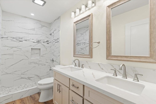 bathroom with a tile shower, wood-type flooring, vanity, and toilet