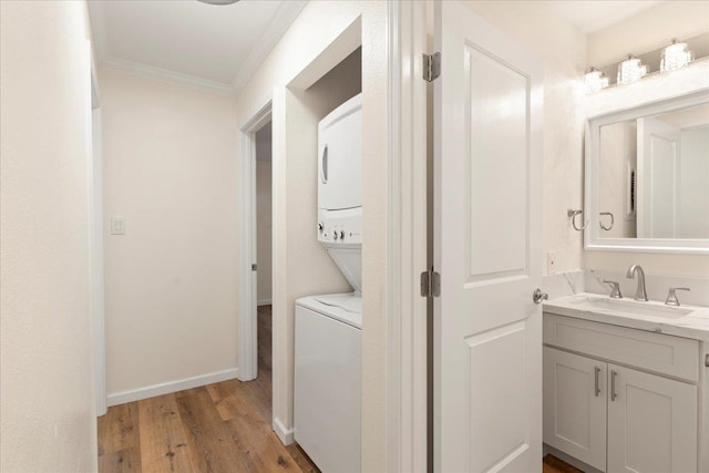 clothes washing area with light hardwood / wood-style flooring, sink, ornamental molding, and stacked washer and clothes dryer