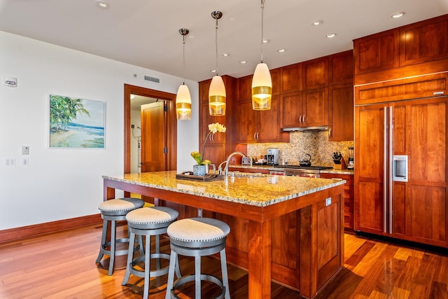 kitchen featuring wood-type flooring, light stone counters, paneled refrigerator, and hanging light fixtures