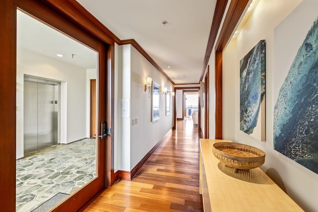 corridor featuring ornamental molding, elevator, and light hardwood / wood-style flooring