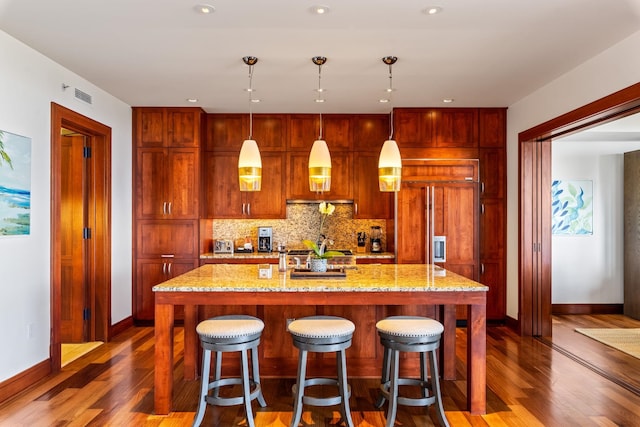 kitchen featuring hanging light fixtures, a kitchen island with sink, backsplash, and dark hardwood / wood-style flooring