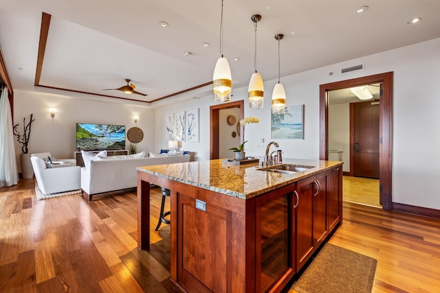 kitchen featuring light stone counters, pendant lighting, light wood-type flooring, beverage cooler, and sink