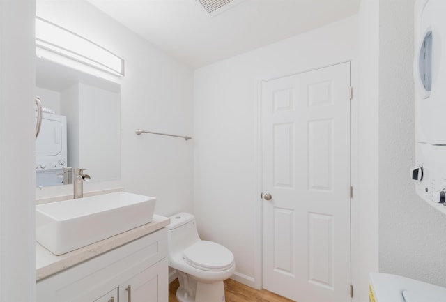 bathroom featuring hardwood / wood-style floors, vanity, toilet, and stacked washer / dryer