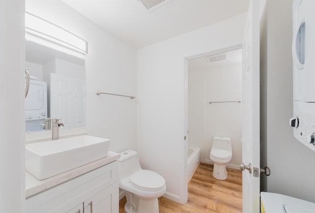 bathroom featuring wood-type flooring, toilet, and stacked washer / dryer