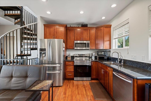 kitchen with light wood-type flooring, a sink, recessed lighting, stainless steel appliances, and dark stone counters