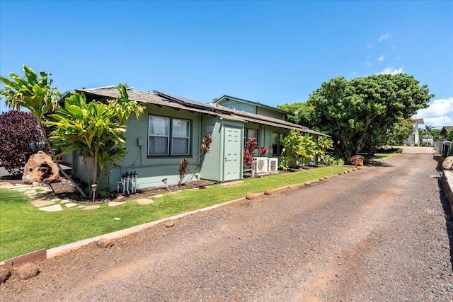 view of front of property featuring dirt driveway, a front yard, and roof mounted solar panels