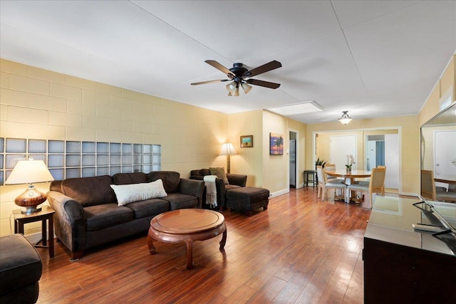 living room featuring ceiling fan, hardwood / wood-style floors, and concrete block wall