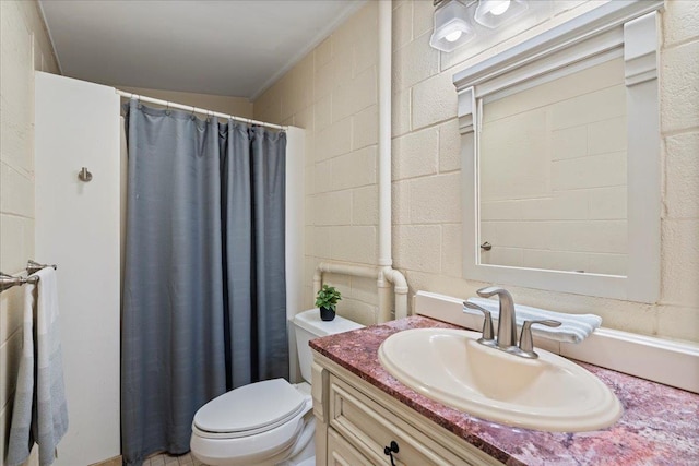 full bathroom featuring a shower with shower curtain, concrete block wall, toilet, and vanity