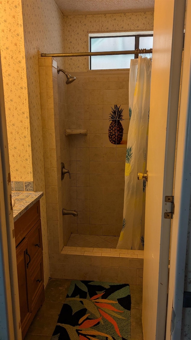 bathroom featuring wallpapered walls, a tile shower, and vanity