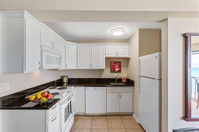 kitchen featuring sink, white cabinetry, dark stone countertops, light tile patterned floors, and white appliances