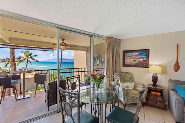 tiled dining space with a water view, ceiling fan, floor to ceiling windows, and a textured ceiling