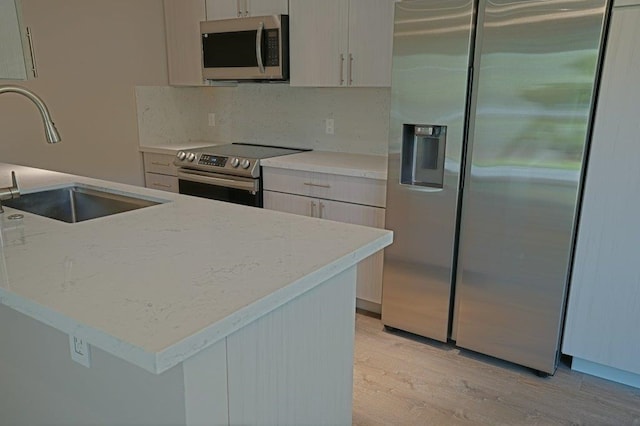 kitchen featuring light stone countertops, appliances with stainless steel finishes, tasteful backsplash, sink, and light hardwood / wood-style floors