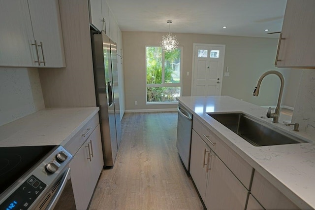 kitchen featuring light wood-type flooring, light stone counters, stainless steel appliances, sink, and a chandelier