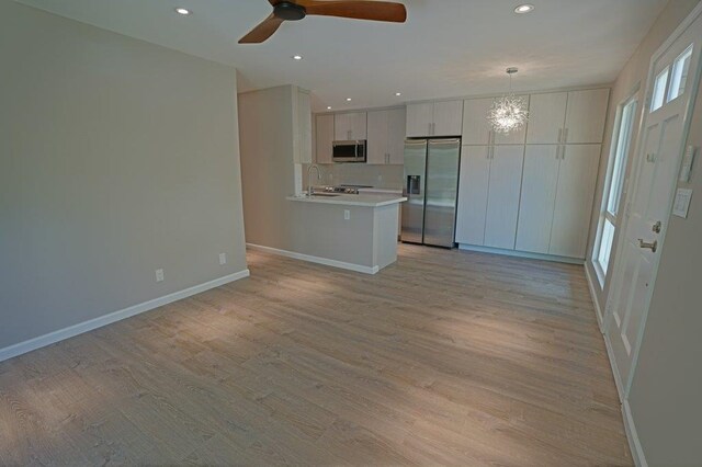 kitchen featuring white cabinets, light wood-type flooring, stainless steel appliances, and hanging light fixtures