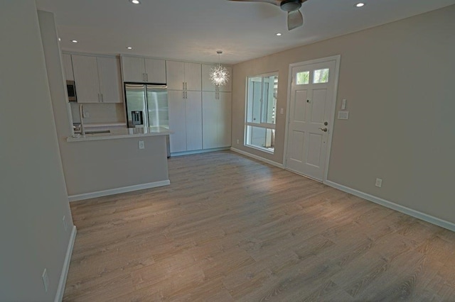 kitchen with stainless steel appliances, pendant lighting, light hardwood / wood-style floors, white cabinets, and ceiling fan with notable chandelier