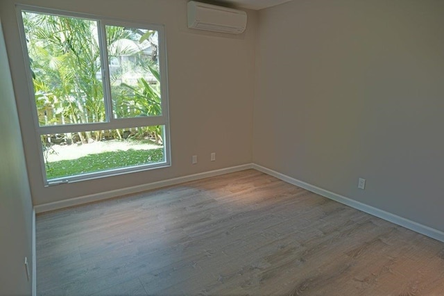 spare room featuring light hardwood / wood-style flooring, an AC wall unit, and plenty of natural light