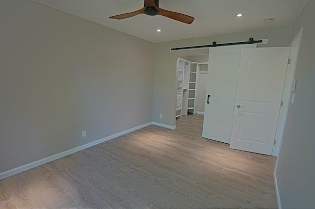 unfurnished bedroom with ceiling fan, a barn door, light wood-type flooring, and a closet