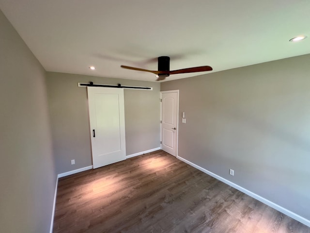 unfurnished bedroom featuring ceiling fan, a barn door, and dark wood-type flooring