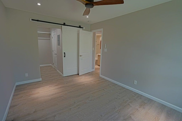 unfurnished bedroom with a closet, a barn door, light hardwood / wood-style floors, and ceiling fan