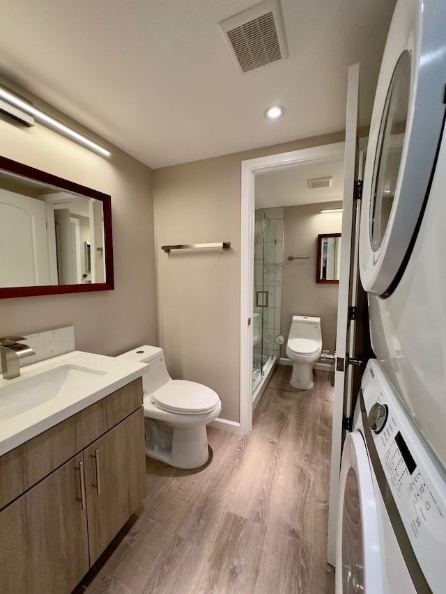 bathroom featuring wood-type flooring, vanity, toilet, and stacked washer / drying machine