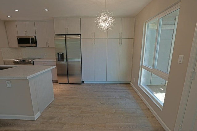 kitchen with white cabinets, decorative light fixtures, light hardwood / wood-style floors, and appliances with stainless steel finishes