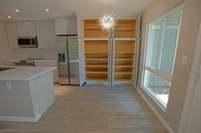 kitchen featuring hanging light fixtures, stainless steel appliances, an inviting chandelier, white cabinets, and light wood-type flooring