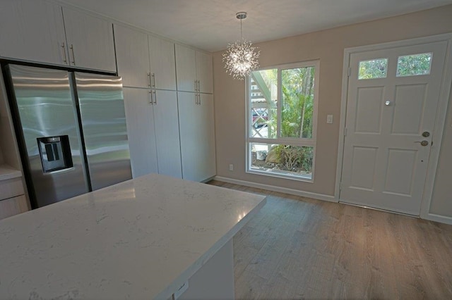 kitchen featuring white cabinets, stainless steel fridge, light wood-type flooring, decorative light fixtures, and light stone counters