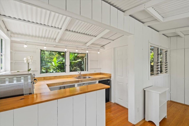 kitchen with light wood finished floors, butcher block countertops, beamed ceiling, dishwasher, and a sink