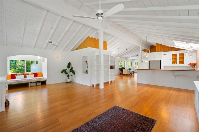 unfurnished living room with light wood finished floors, arched walkways, vaulted ceiling with beams, and ceiling fan