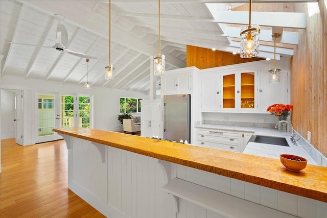 kitchen featuring light wood-type flooring, stainless steel refrigerator, a sink, a peninsula, and glass insert cabinets