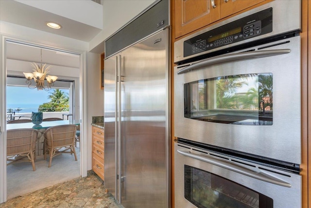 kitchen with light carpet, appliances with stainless steel finishes, stone countertops, decorative light fixtures, and a chandelier