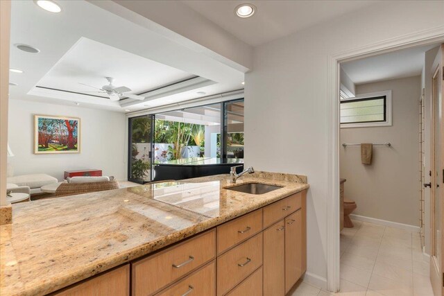 bathroom with a raised ceiling, vanity, toilet, and ceiling fan