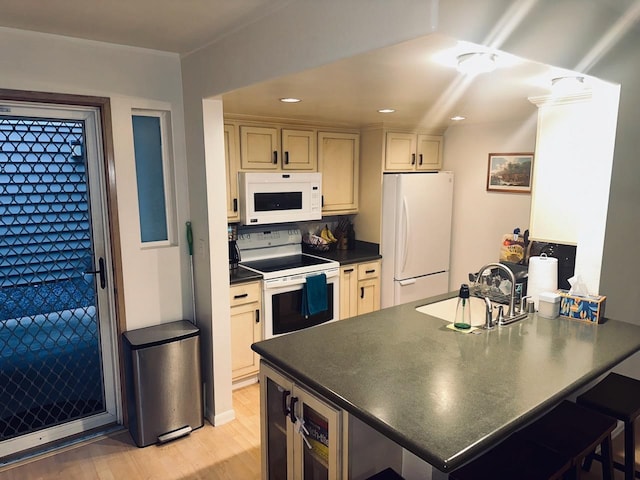 kitchen featuring a kitchen bar, sink, light hardwood / wood-style flooring, kitchen peninsula, and white appliances