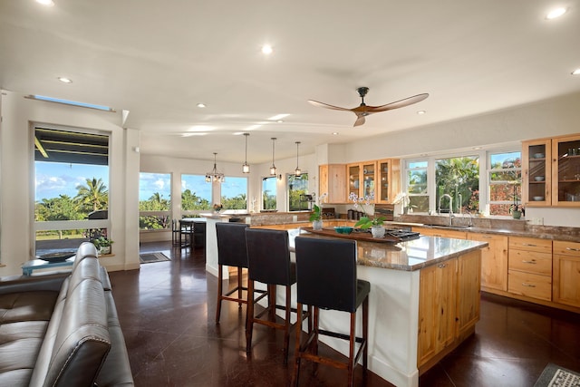 kitchen with glass insert cabinets, light brown cabinets, a sink, a kitchen island, and a kitchen breakfast bar