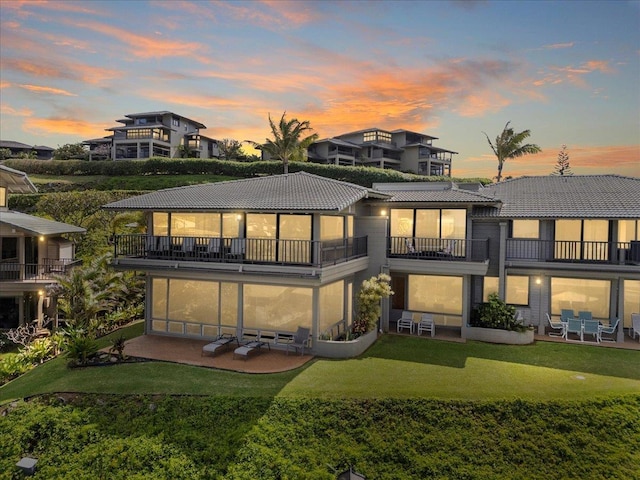 rear view of property featuring a balcony, a tiled roof, a lawn, and a patio