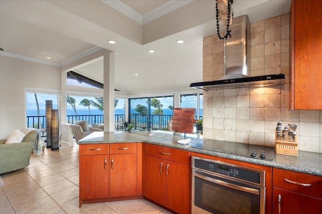 kitchen featuring oven, decorative backsplash, ornamental molding, and wall chimney range hood