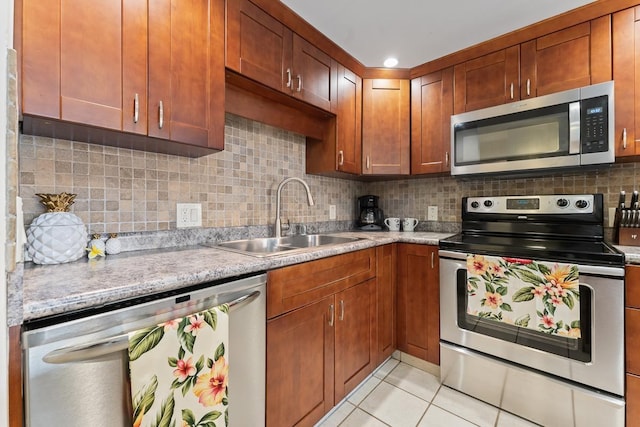 kitchen featuring light tile patterned floors, stainless steel appliances, tasteful backsplash, brown cabinetry, and a sink